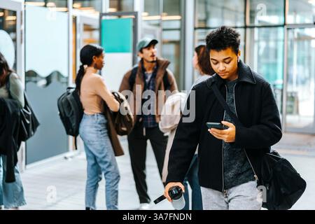 Young man carrying bag using smart phone while walking in tech university campus Stock Photo