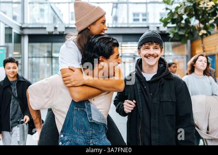 Cheerful young man piggybacking female friend while walking in college campus Stock Photo