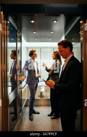 Male and female business colleagues talking with each other while standing in elevator at office Stock Photo