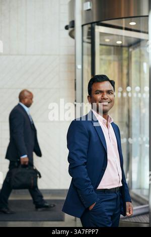 Portrait of smiling male entrepreneur standing with hand in pocket at office lobby Stock Photo
