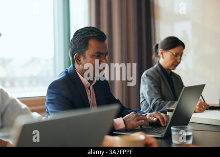 Focused businessman working on laptop while sitting with colleagues in office Stock Photo