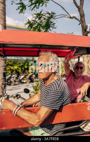 Senior man wearing sunglasses sitting with boyfriend in pedicab Stock Photo
