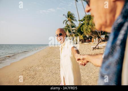 Happy senior man holding hands of boyfriend while standing on beach at sunny day Stock Photo
