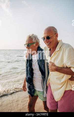 Happy senior gay man walking with arm around boyfriend on beach Stock Photo