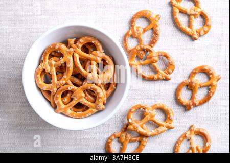 Salted pretzels in a white bowl on linen fabric. Golden toasted small pretzels of traditional shape with intertwined ends to form a pretzel bow. Stock Photo