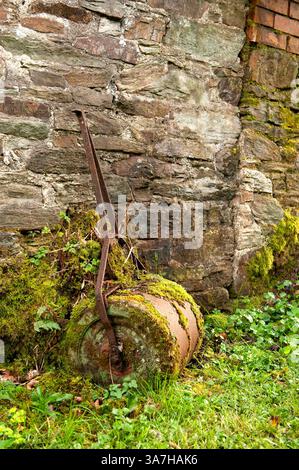 Old, rusty lawn roller lying forgotten and overgrown against an old stone wall in Cornwall, England, UK Stock Photo