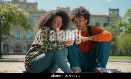 African American couple man woman friends students male female girl guy together in city outdoors looking mobile phone using smartphone reading bad Stock Photo