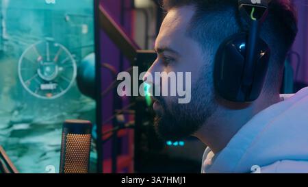 Serious concentrated Caucasian addicted man male guy gamer evening home playing video game shooting entertainment focused internet gaming battle Stock Photo