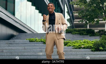Happy successful excited fast running on office stairs building company walk African American man guy male businessman business in city celebrate Stock Photo