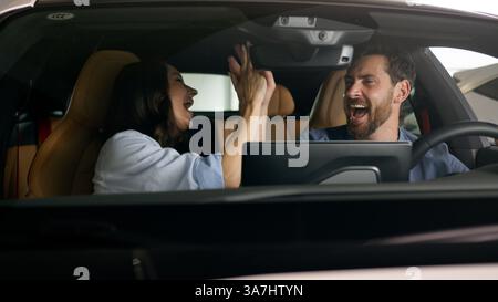 Caucasian couple dancing happy inside automobile celebrate buying auto joyful driving trip travel dance give high five fun man guy male boyfriend Stock Photo