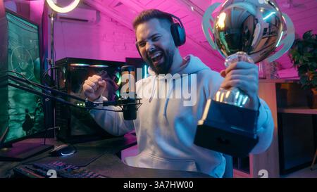 Happy smiling Caucasian man male guy gamer playing laptop addiction play online video game internet computer at night neon sport streaming win victory Stock Photo
