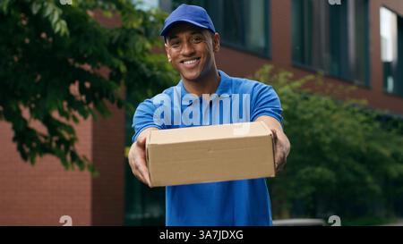 Happy African American smiling man delivery guy male courier holding box package shop store parcel delivery purchase cargo transaction in city Stock Photo