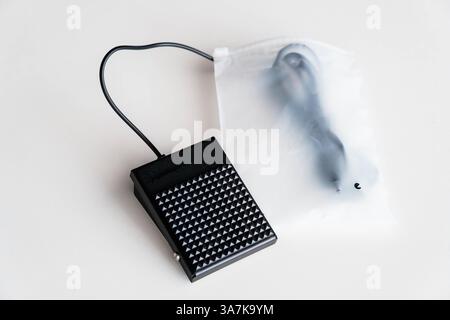 Black Electric Sewing Machine Foot Pedal Controller and Cable in Translucent Plastic Packaging on White Surface. Stock Photo