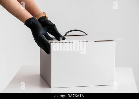 Hands in Black Gloves Carefully Closing White Cardboard Box on White Table. Stock Photo