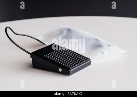 Black Foot Switch Pedal with Cable on White Surface Near Transparent Sterile Bag. Stock Photo