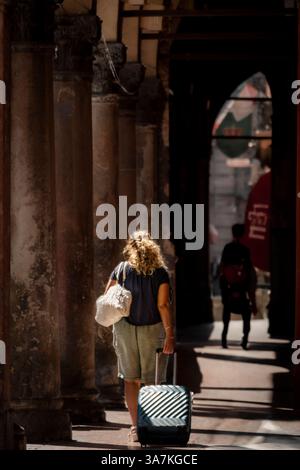 Blonde woman with a trolley bag walking in a tourist destination in Italy. Stock Photo