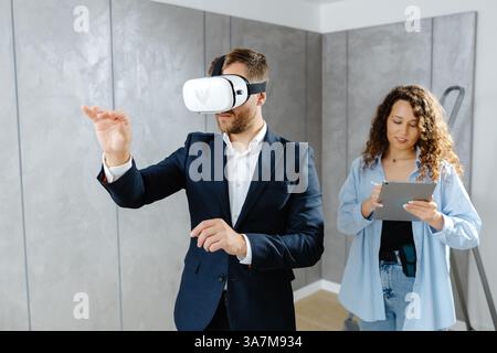 Man client wearing VR glasses imagining future interior standing with designer at the construction site. The concept of repair on a modern design Stock Photo