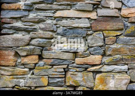 Rustic stone wall featuring an array of gray and beige stones, providing a textured surface perfect for construction and design purposes. Stock Photo