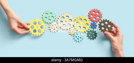 Hands and wooden gears on light blue background, top view Stock Photo