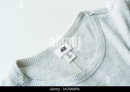 Close-up of H&M brand label and size tag on a grey waffle-knit shirt collar, isolated on white. NY, NY-USA - Marth 27 2025 Stock Photo