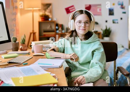 Portrait of female student with prosthetic arm and headphones sitting at desk with laptop and notes spread out Stock Photo