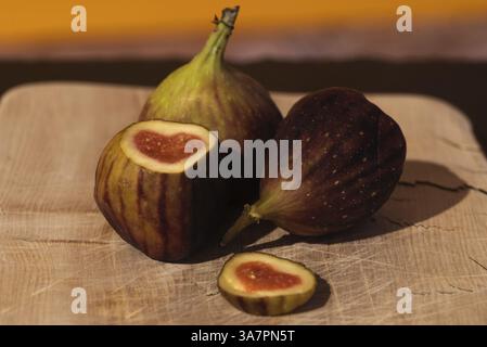 Three figs, one cut open, with a heart-shaped centre on a wooden board against a yellow background, Germany, Europe Stock Photo