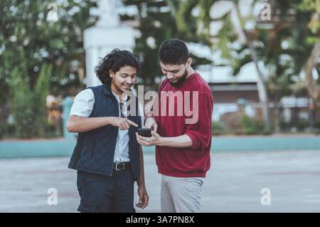 Two young friends holding and having fun with the phone outdoors. Two happy guys looking at cell phone on the street Stock Photo