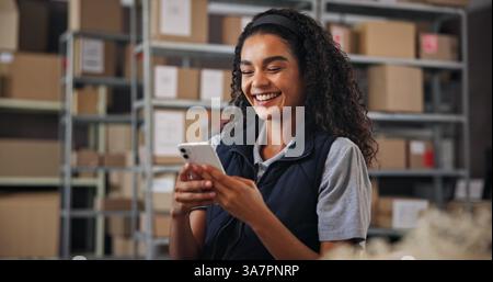 Supply chain, woman and happy with phone for delivery, distribution and success for ecommerce. Small business, warehouse and excited owner with Stock Photo