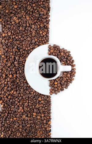 Minimalist composition of a cup of black coffee on a saucer, surrounded by roasted coffee beans on a split white and textured background. Stock Photo