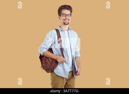 Portrait of happy smiling smart guy student with backpack and textbook on beige background. Stock Photo