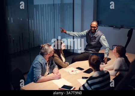 A diverse team of young professionals collaborates in a modern office conference room. Businesspeople discuss strategy, technology, and planning Stock Photo