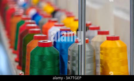 A row of colorful spools of thread are on display. The spools are of various colors, including green, yellow, and red. The spools are arranged in a ne Stock Photo