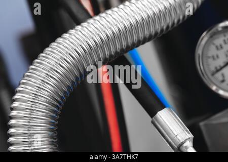 A long silver corrugated stainless steel high pressure pipe with a black hose attached to it. The hose is connected to a pressure gauge measuring the Stock Photo