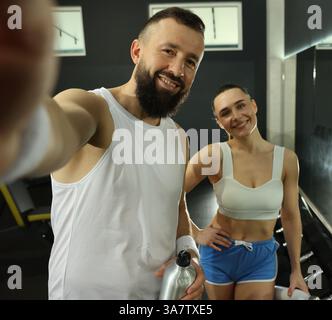 Couple with water bottles taking selfie after training in gym Stock Photo