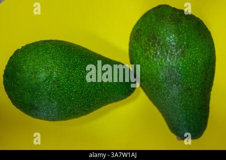 Two fresh, whole avocados sit on a bright yellow backdrop, creating a bold visual contrast Stock Photo