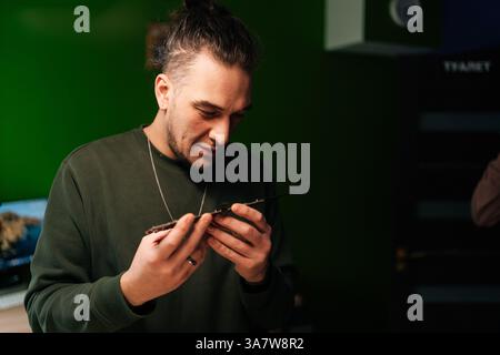 Portrait of skilled repairman master examining laptop motherboard, troubleshooting issues in professional electronics repair workshop with green wall. Stock Photo