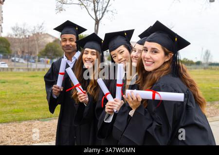 Group of cheerful multiethnic graduates wearing academic gowns and holding diplomas celebrating their graduation Stock Photo