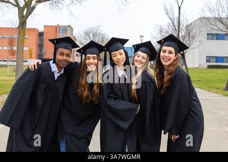 Multiethnic group of students wearing graduation gowns and caps celebrating their graduation at the university campus Stock Photo