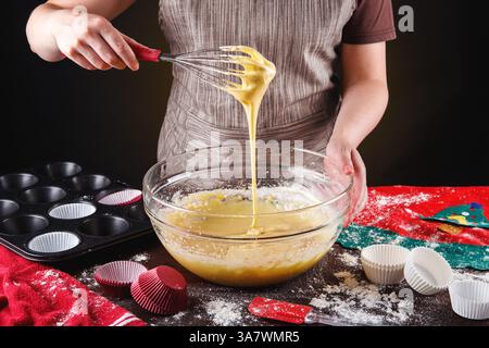 Crop anonymous housewife with whisk mixing dough in glass bowl while making delicious sweet cupcakes for Christmas celebration Stock Photo