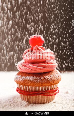Closeup of delicious sweet cupcake with pink frosting and red cherry sprinkled with white sugar powder served for Christmas celebration Stock Photo