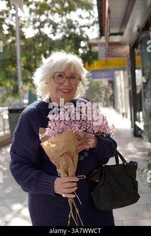 smiling elderly senior woman with bouquet of flowers in the street Stock Photo