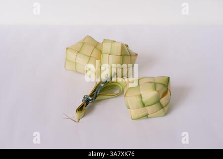 A trio of ketupat, traditional rice dumplings, sits on a plain white surface. These iconic woven packets, crafted from young coconut leaves, are an es Stock Photo