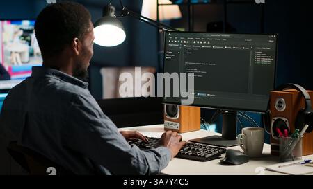 Black man programmer manages code and scripts in artificial intelligence and machine learning on dual monitors computer setup. Male freelancer uses pc to guarantee cyber security. Camera B. Stock Photo