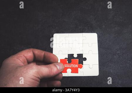 A person is holding a puzzle piece with the word "solution" on it. Concept of problem-solving and the importance of finding a solution Stock Photo