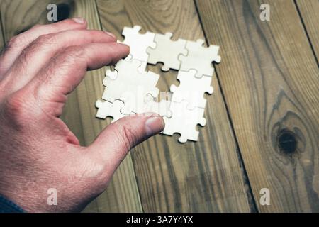 A hand is holding a puzzle piece that is missing. The puzzle is a square with four pieces missing. Scene is one of frustration and determination, as t Stock Photo