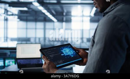 Close up of computer scientist in data center uses AI on tablet, verifying compliance of racks. IT expert using artificial intelligence on device to optimize resource utilization, camera B Stock Photo