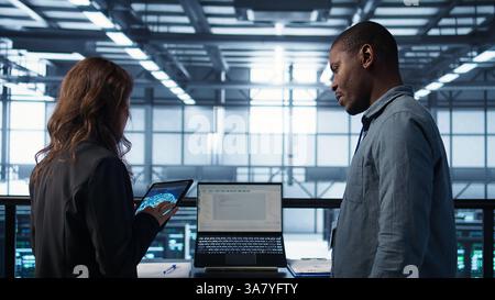 Programmers using AI technology on laptop and tablet in data center employing machine learning models. Devices used by artificial intelligence IT experts in server farm, camera B Stock Photo