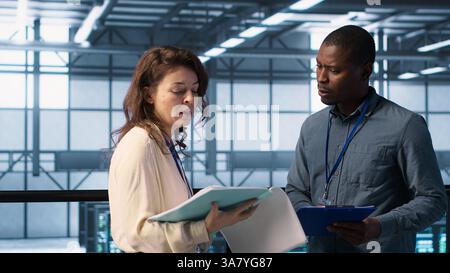 Cheerful admins meeting in data center to review reports and files, doing handshake. Server room employee saluting colleague, doing troubleshooting to prevent downtime, camera A Stock Photo