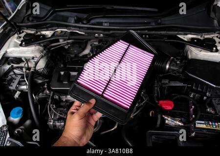 New air filter replacement by auto mechanic in auto repair garage , Hand holding car air filter over engine bay , Car maintenance concept Stock Photo