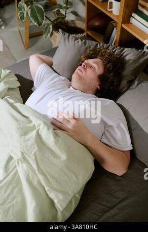 Sleeping Man Resting in Cozy Bed with Green Blanket Stock Photo